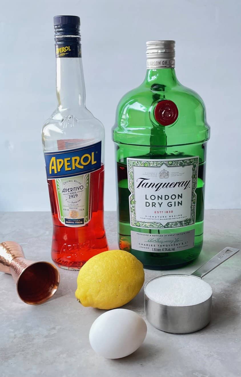 bottles of aperol and gin and other ingredients for aperol sours on a countertop.