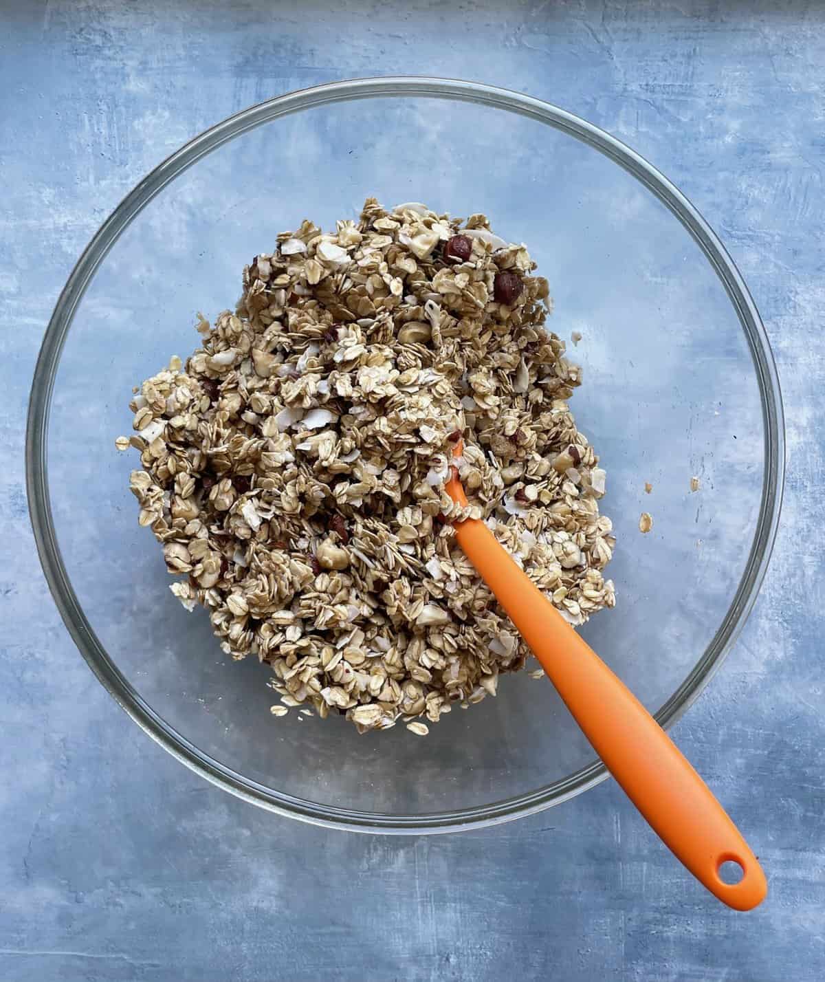 mixed ingredients for homemade gourmet granola and orange silicone spatula in glass bowl. 