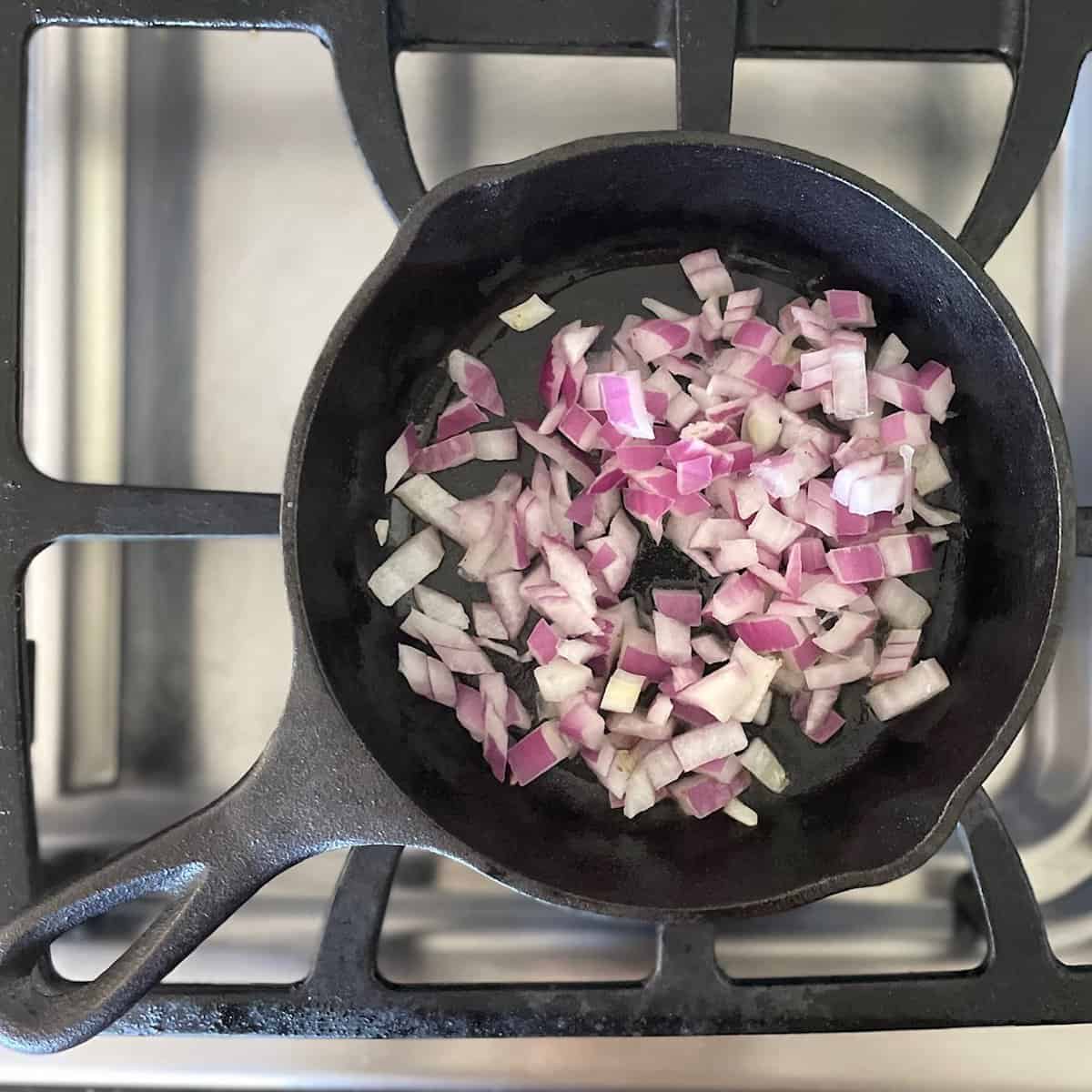 cast iron pan with chopped purple onions on stove top.