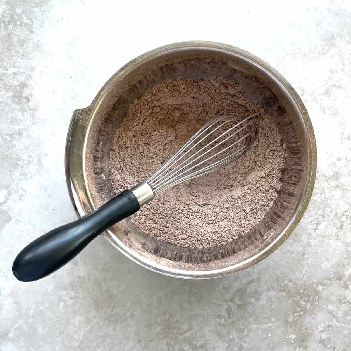 metal bowl of pale brown flour, cocoa, and espresso powder with a metal whisk.