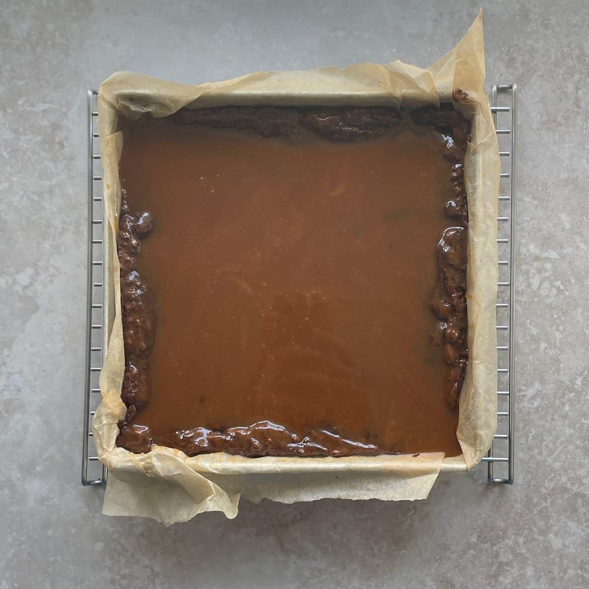pan of espresso brownies covered in liquid caramel in a pan lined with parchment paper.