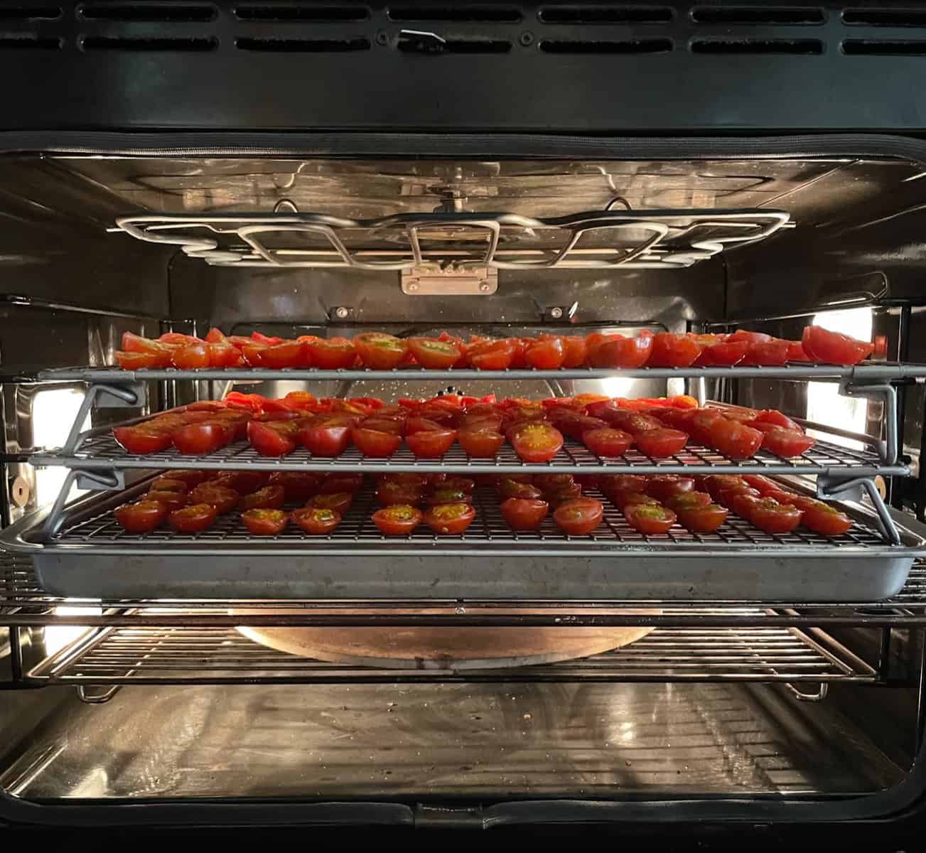 three racks of cherry tomatoes drying in an oven.