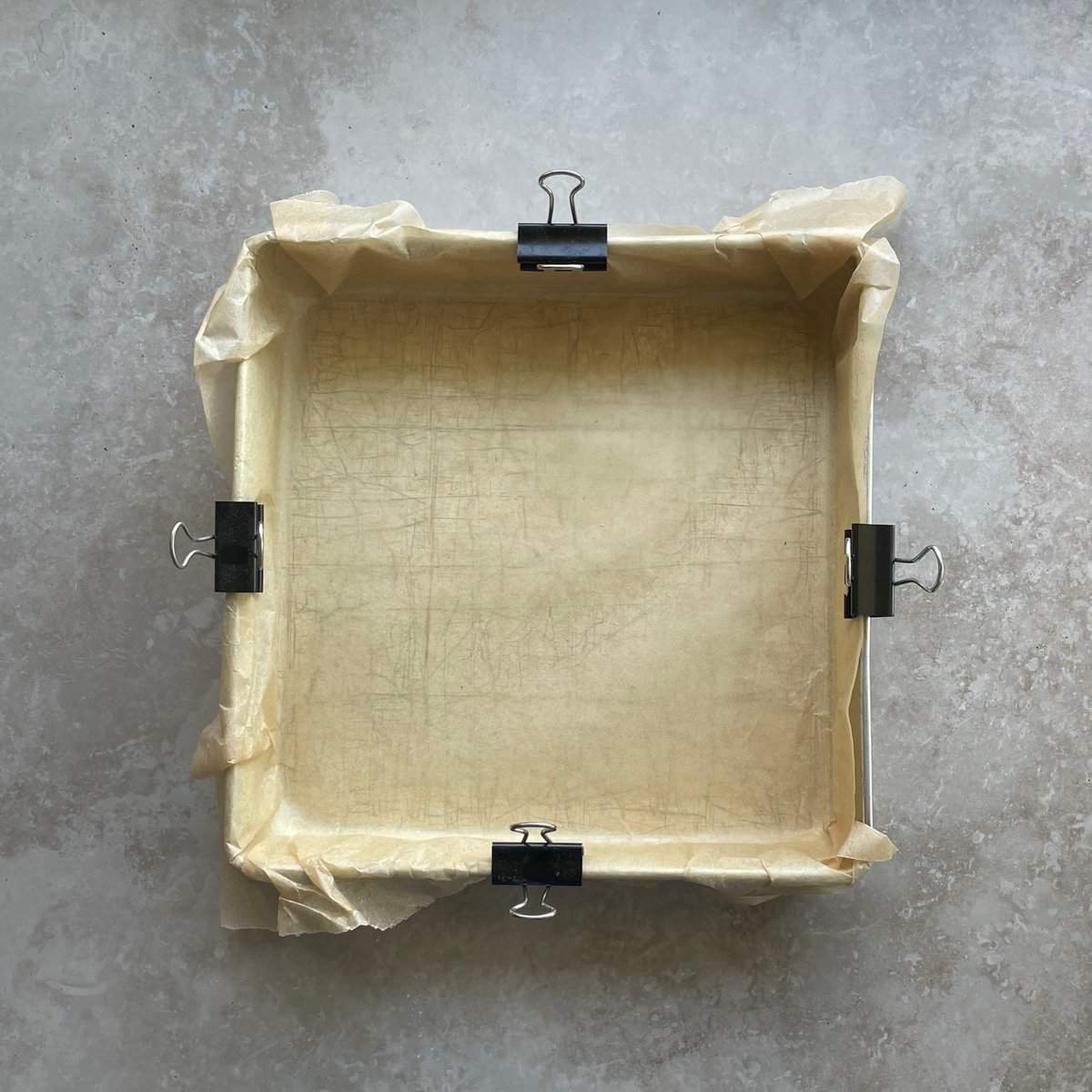 square baking pan lined with parchment paper held in place with binder clips.