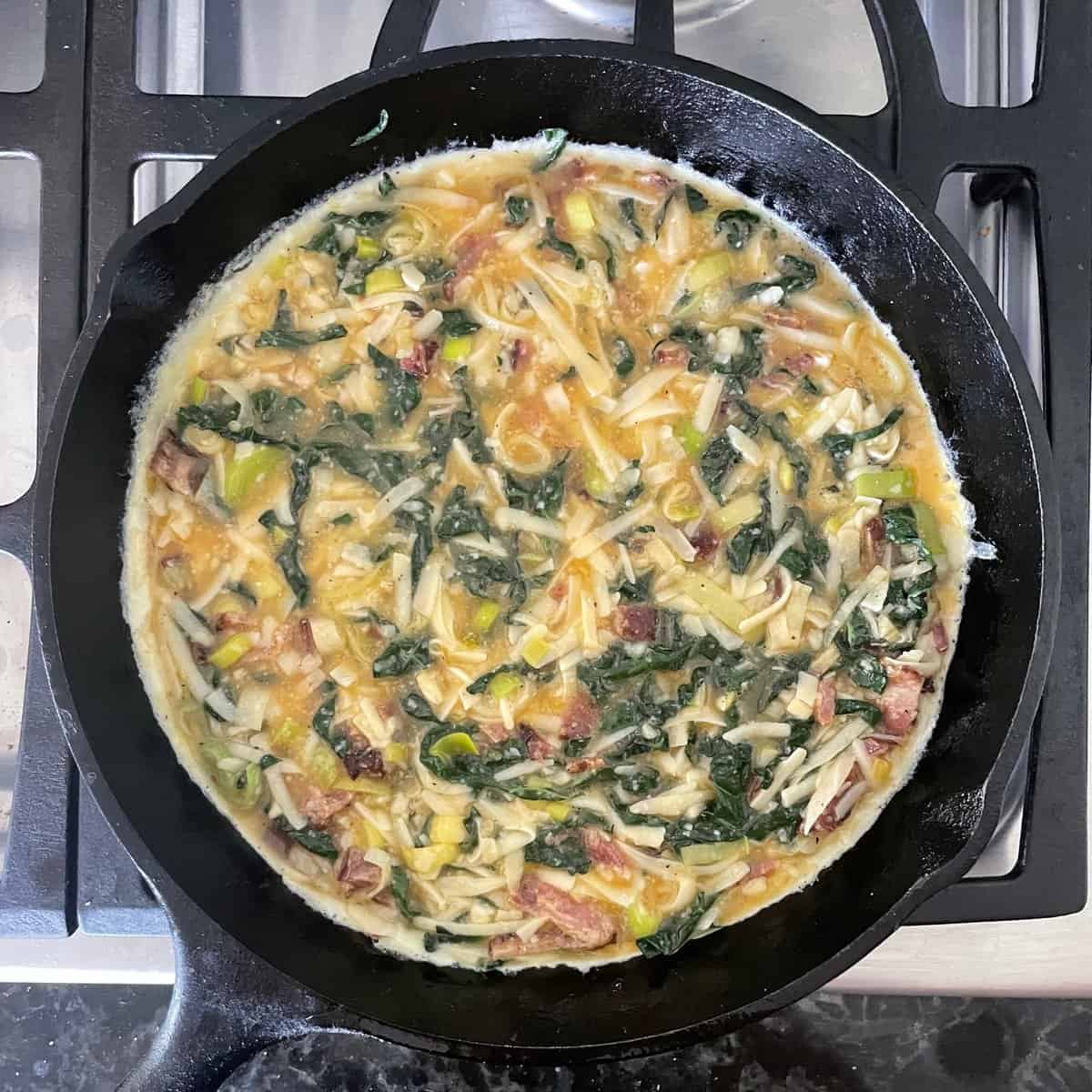bacon, kale, and leek frittata mixture in the cast iron skillet ready for baking.