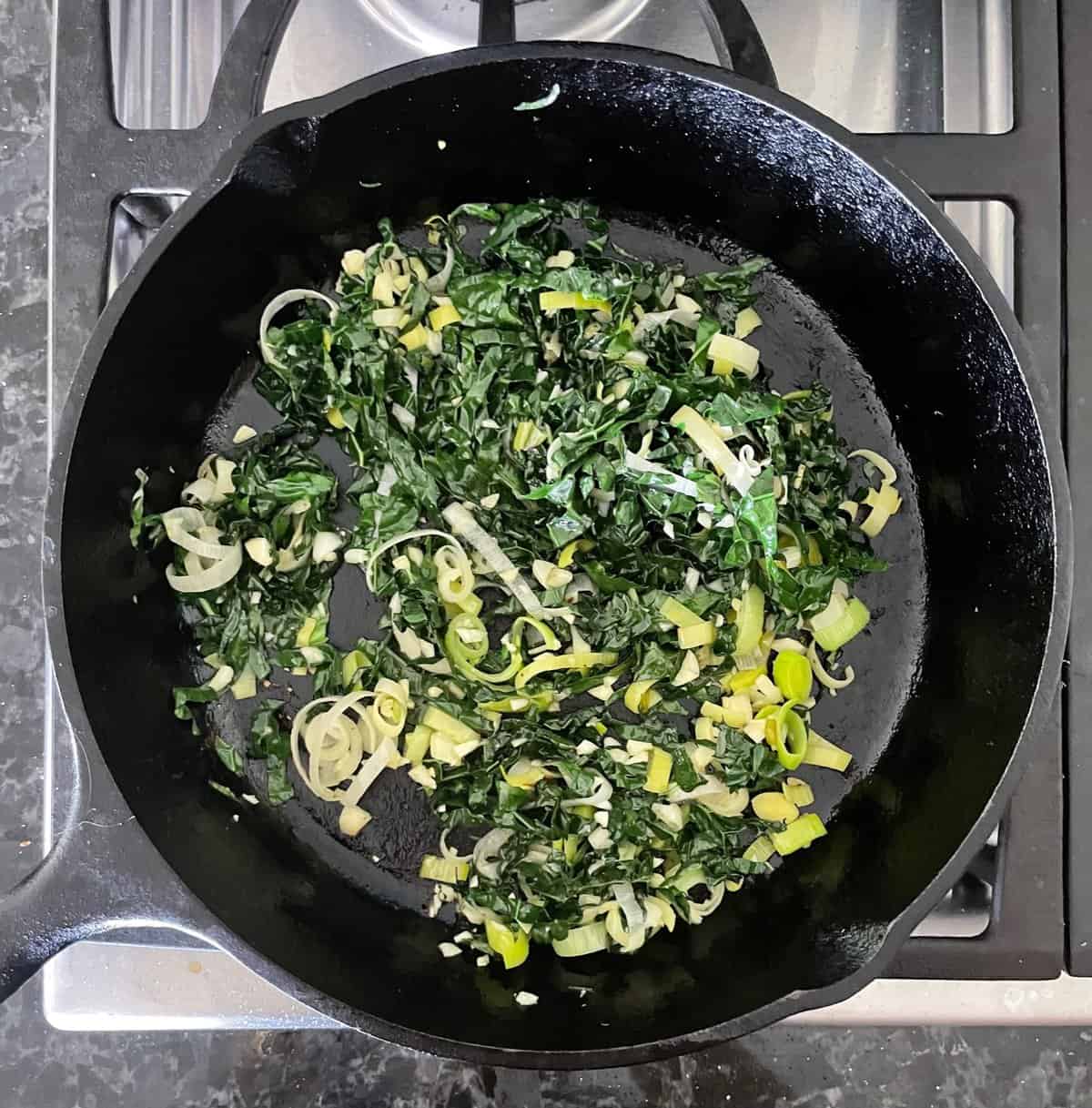 kale and leeks cooking in a cast iron skillet.