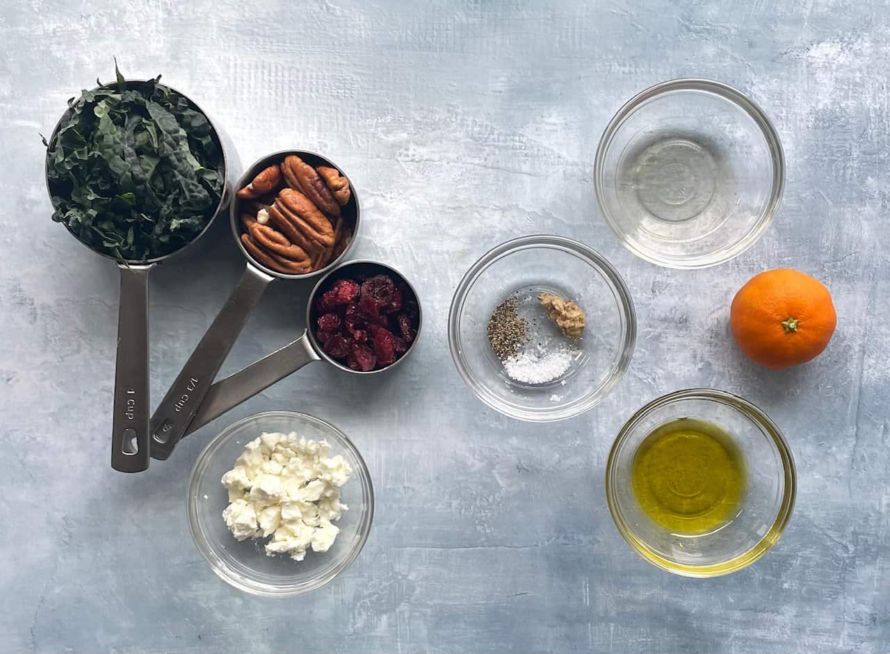 feta, kale, cranberries, pecans, orange and other ingredients on a countertop.