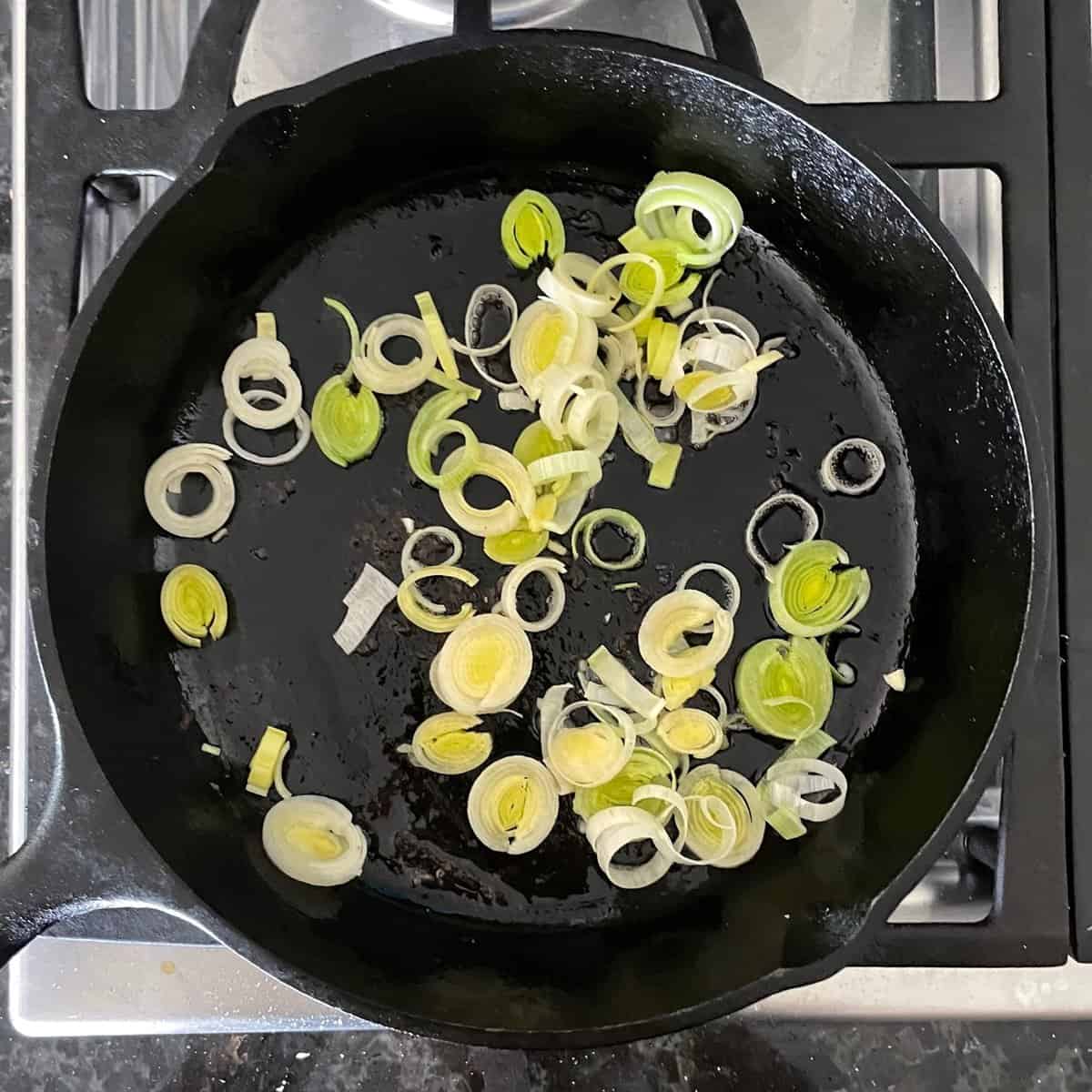 slices of leek cooking in a cast iron skillet.