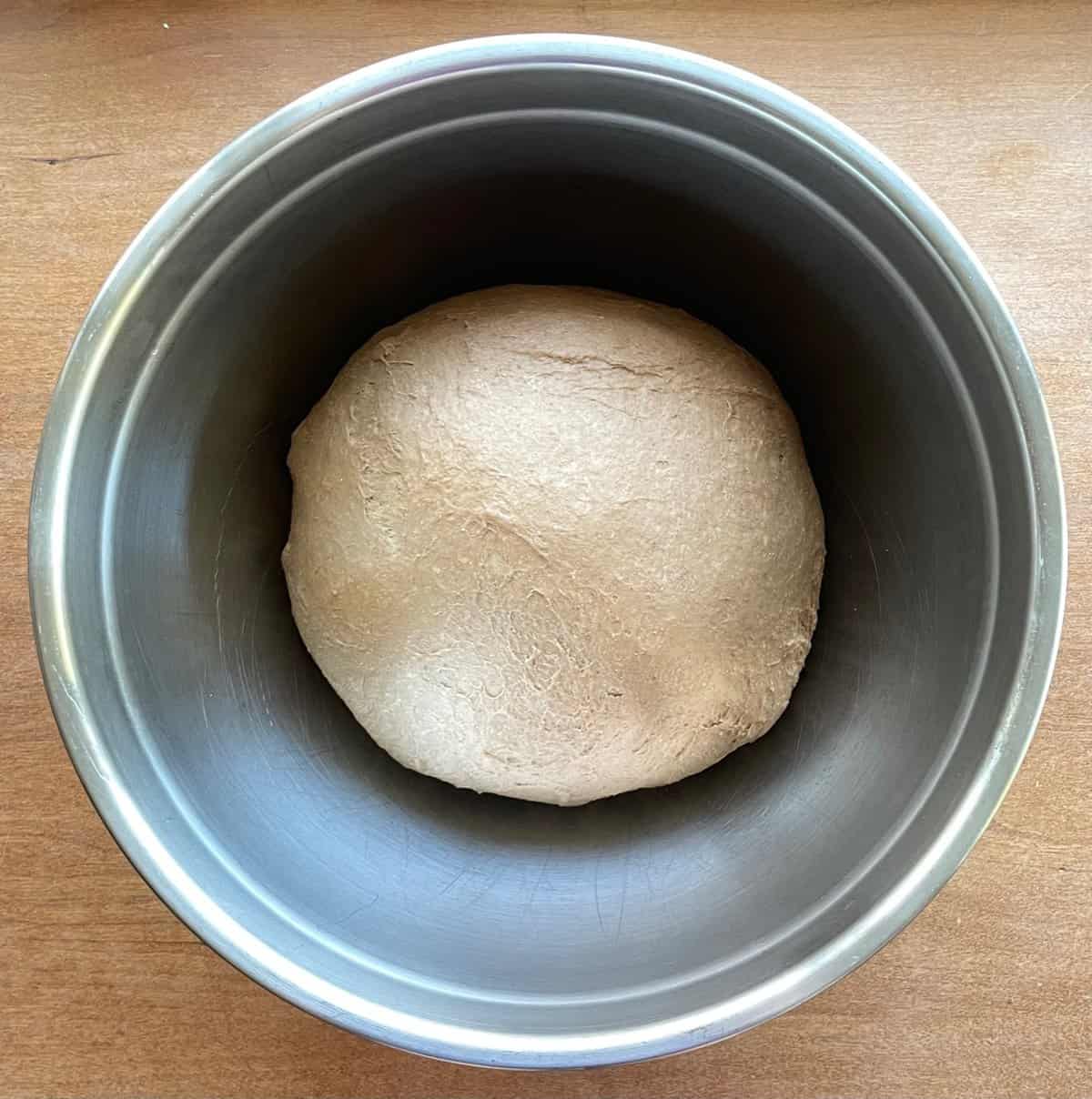 ball of brown bread dough in a mixing bowl after rising.