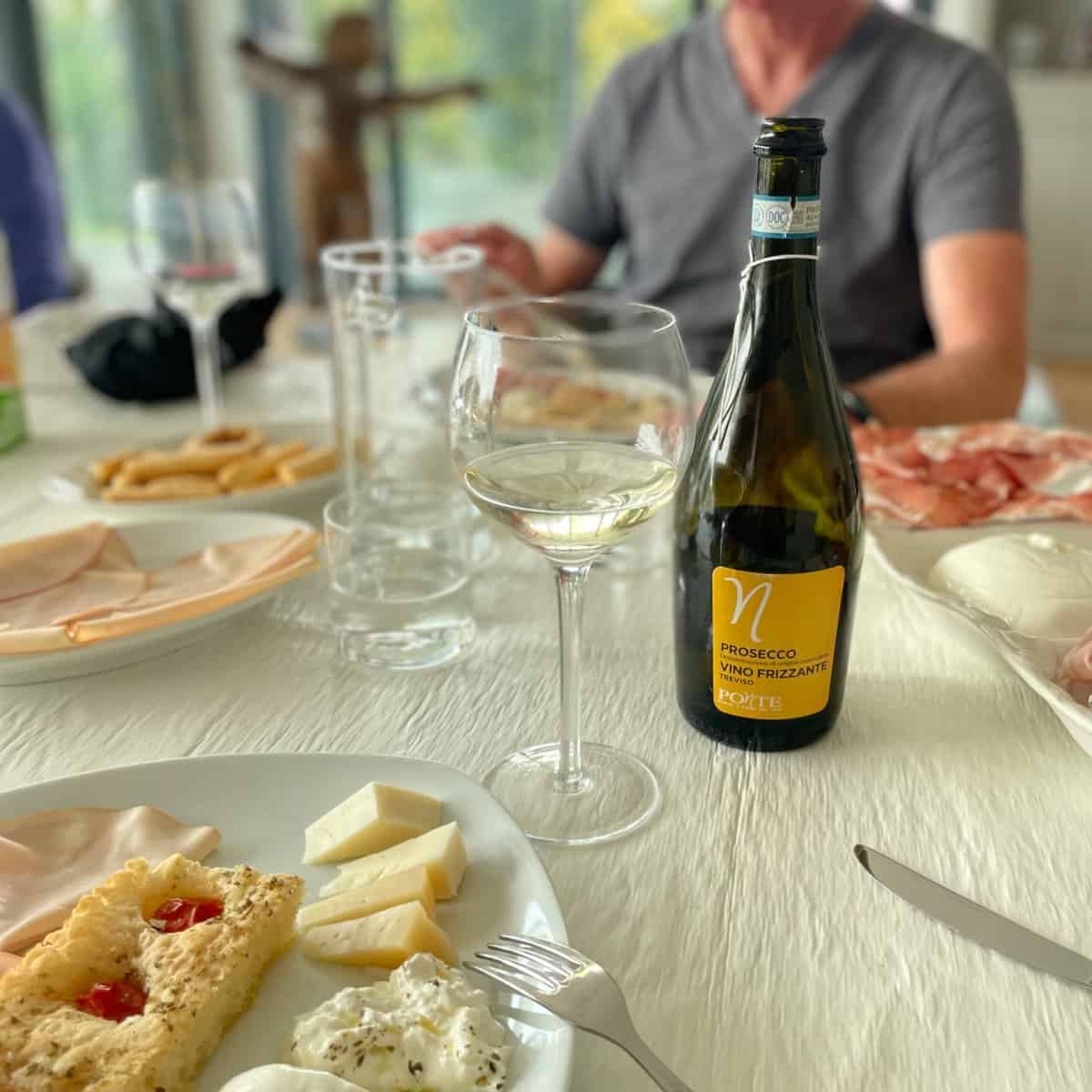 Glass and bottle of Prosecco with plates of meats, cheeses, and focaccia.