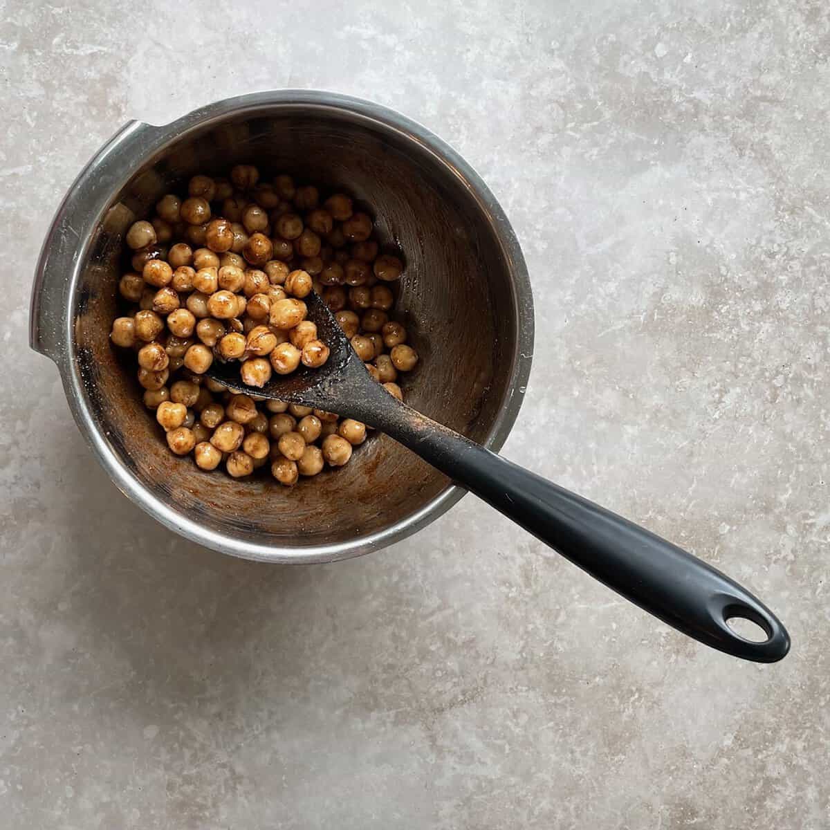 pumpkin pie spice coated chickpeas in a metal bowl with silicone spatula.