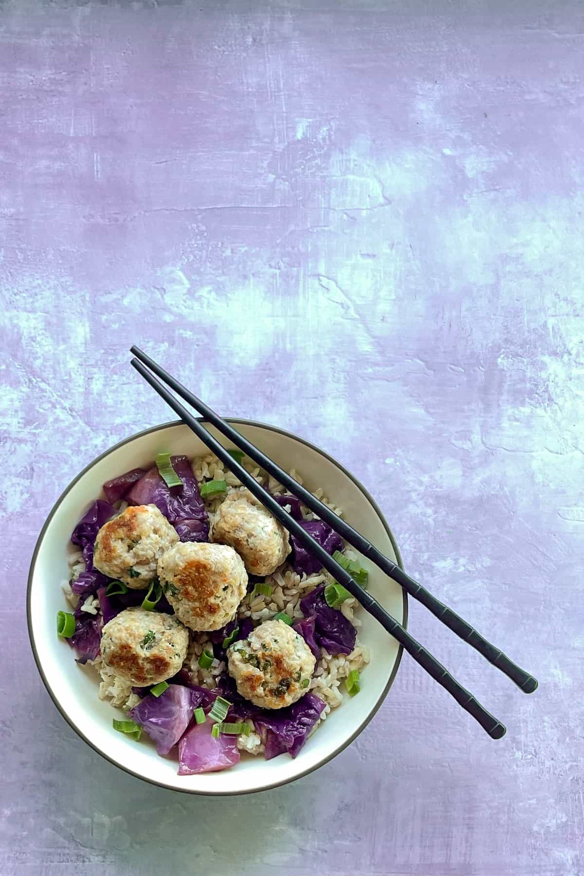 shrimp and pork meatballs in a bowl with rice, pickled cabbage, green onions, and chopsticks.