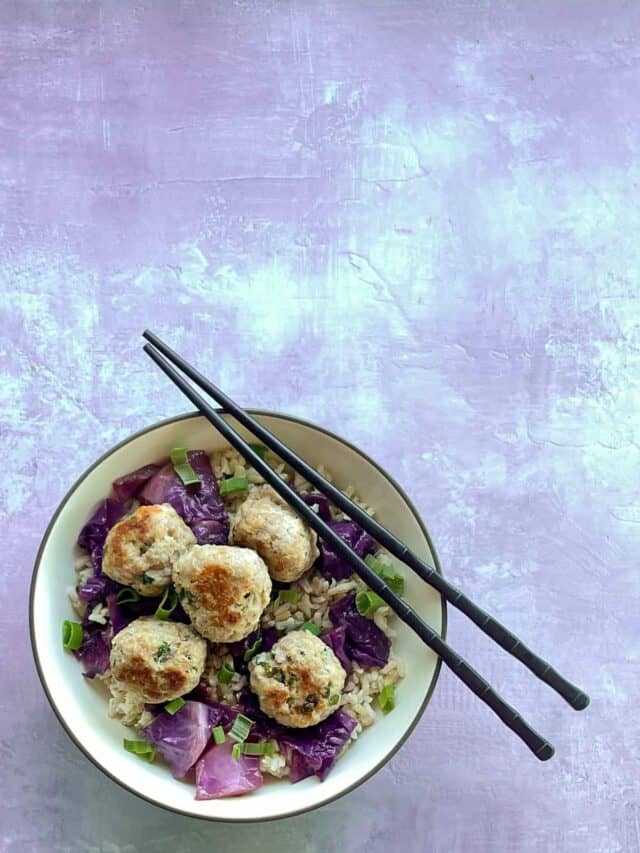 shrimp and pork meatballs in a bowl with rice, pickled cabbage, green onions, and chopsticks.