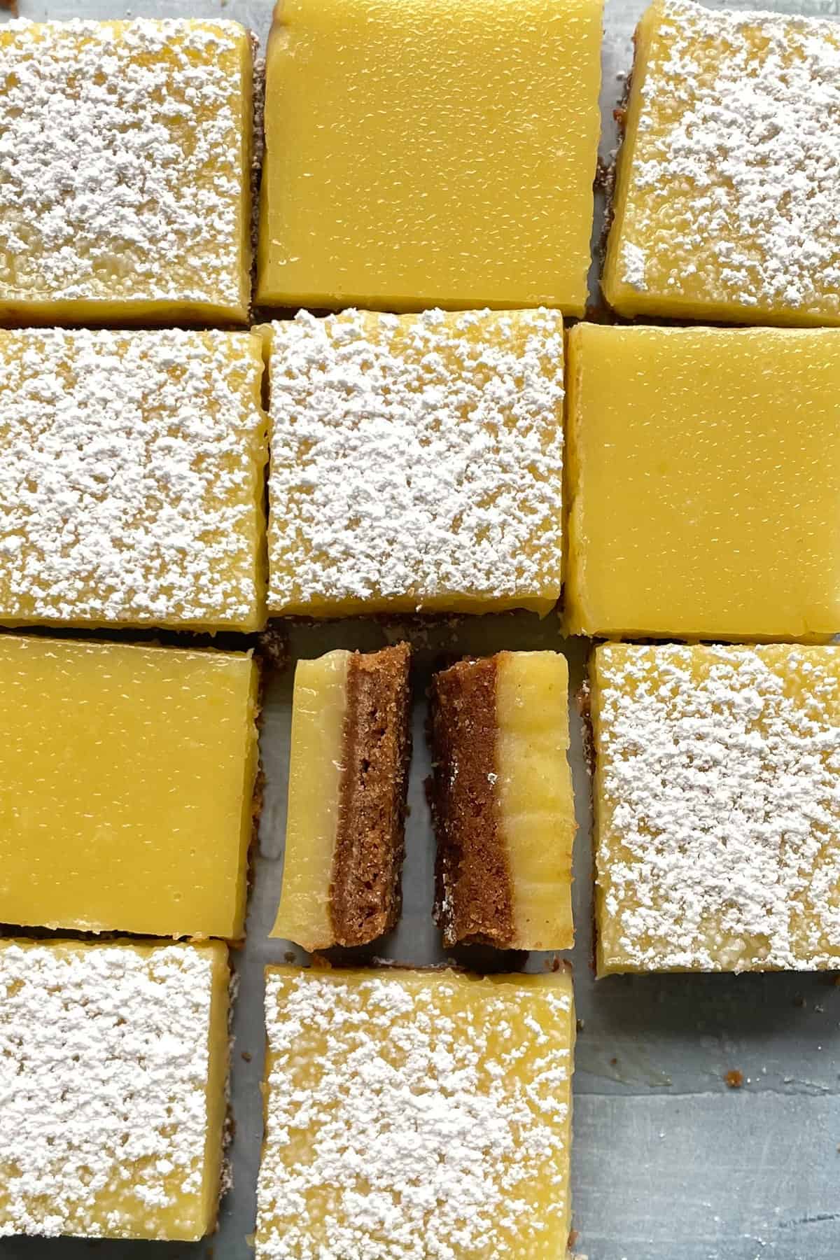 lemon squares on a counter, some dusted with powdered sugar and one turned on its side.