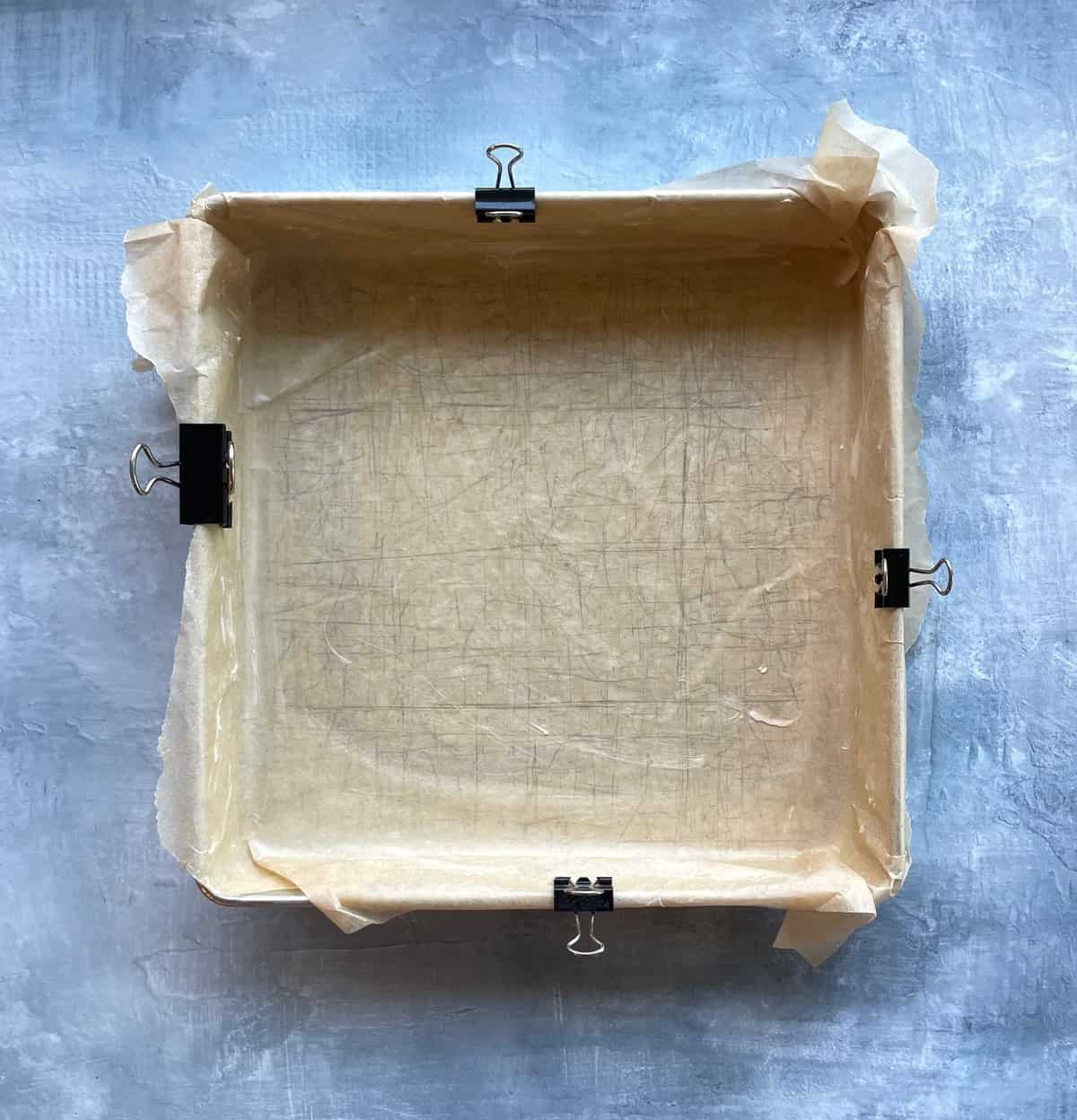 square baking pan lined with parchment paper secured with binder clips.