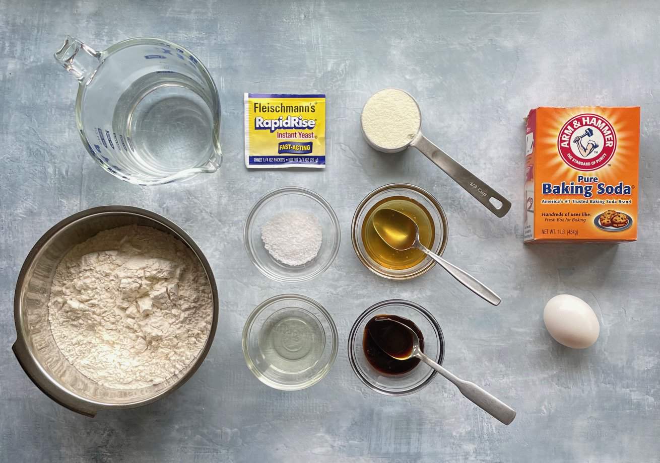 flour, yeast, malt syrup, honey, and other bread ingredients on a countertop.