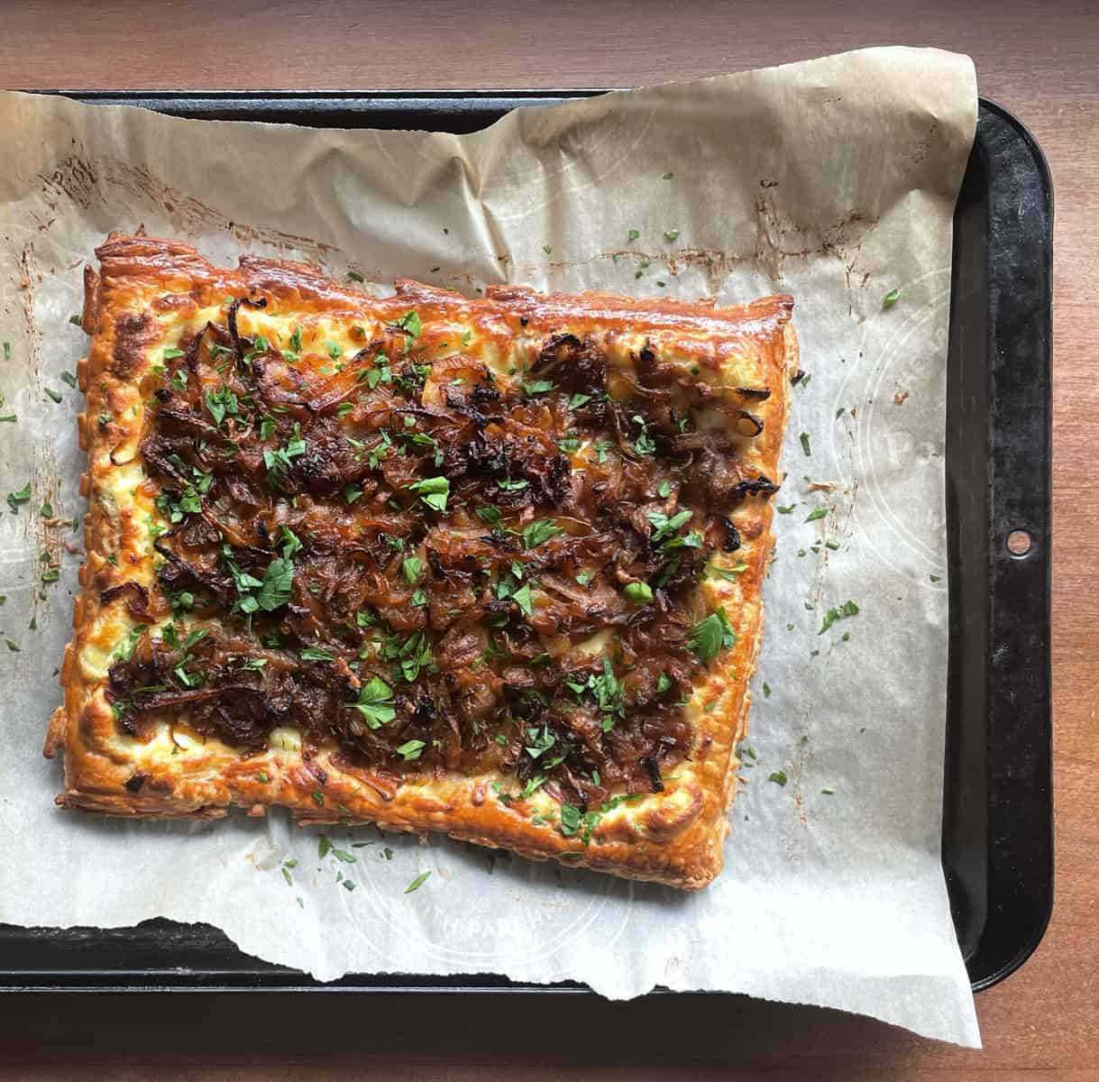 caramelized onions on a rectangular puff pastry tart on parchment on a baking sheet.