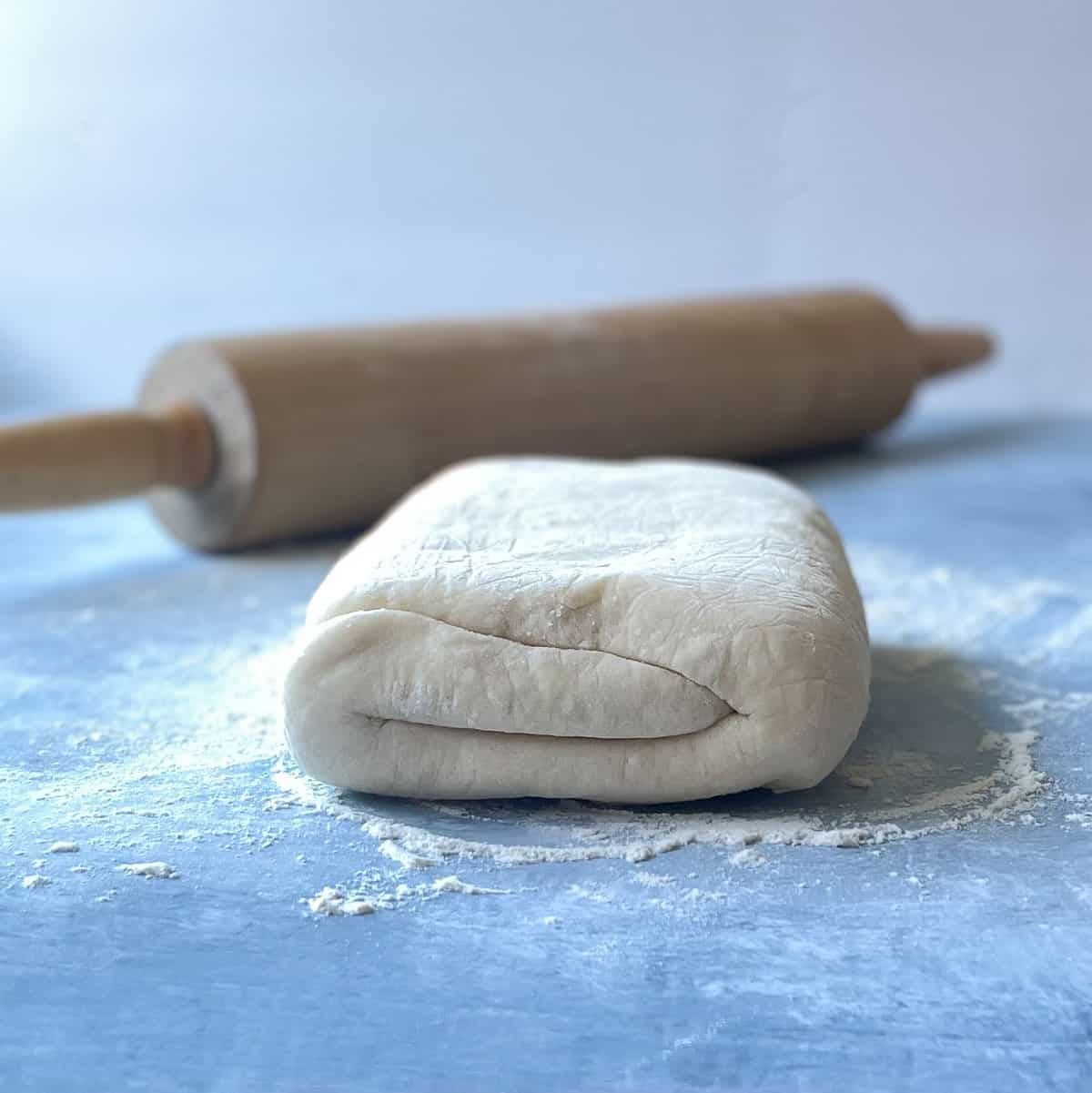 folded puff pastry and rolling pin on flour-dusted countertop.