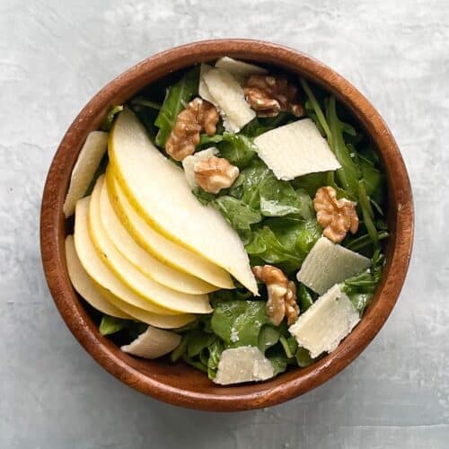 rocket pear salad with toasted walnuts and shaved Parmesan in a small wood salad bowl.