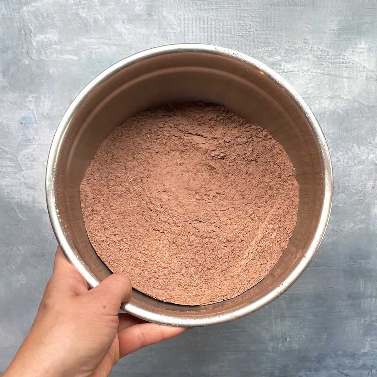hand holding metal bowl of mixed cocoa and flour.