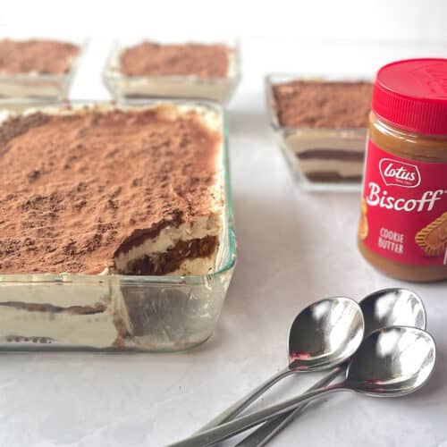clear dish with cocoa dusted tiramisu minus scoopful next to jar of Biscoff cookie butter and spoons.