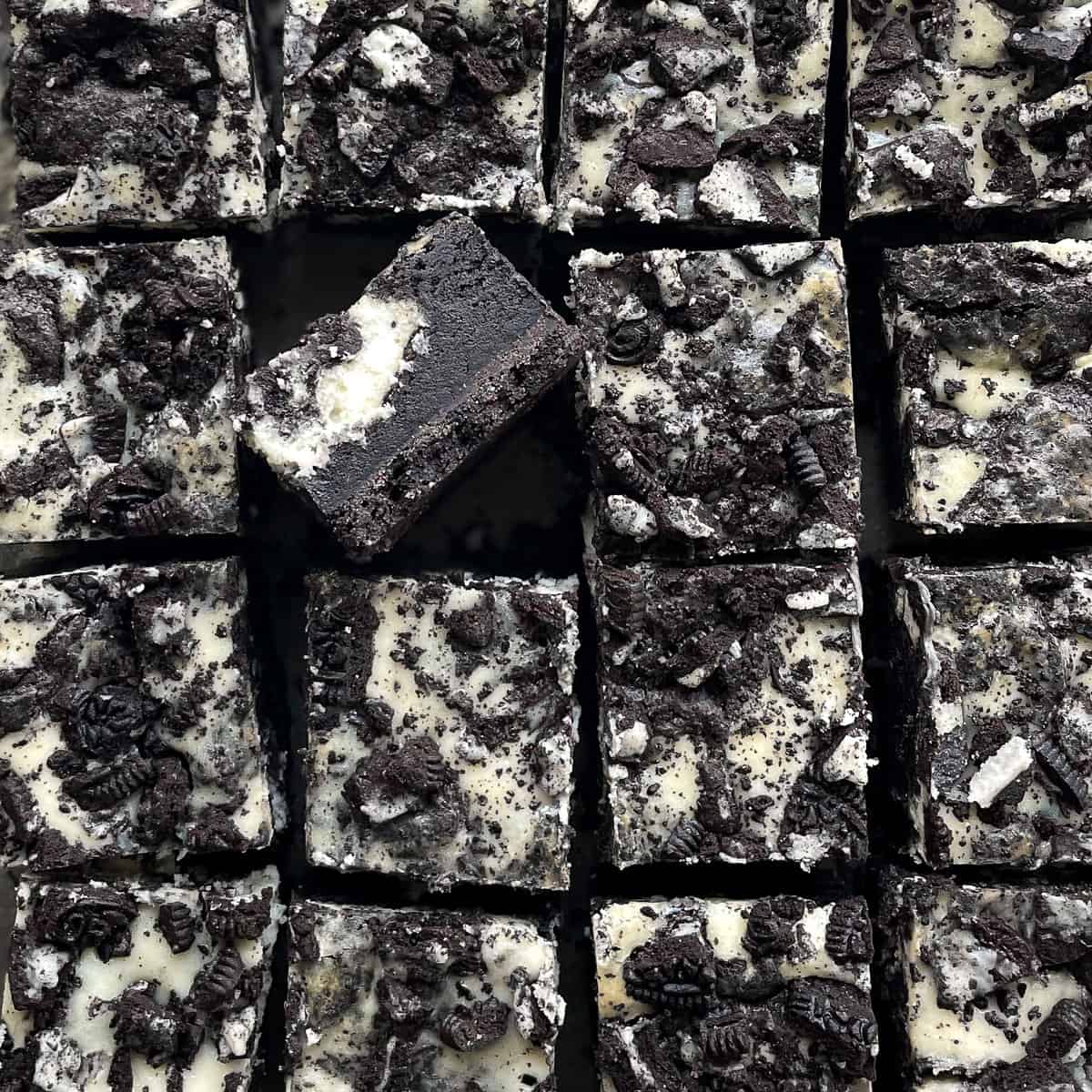 sixteen cut oreo cheesecake brownies with one showing layers on its side.