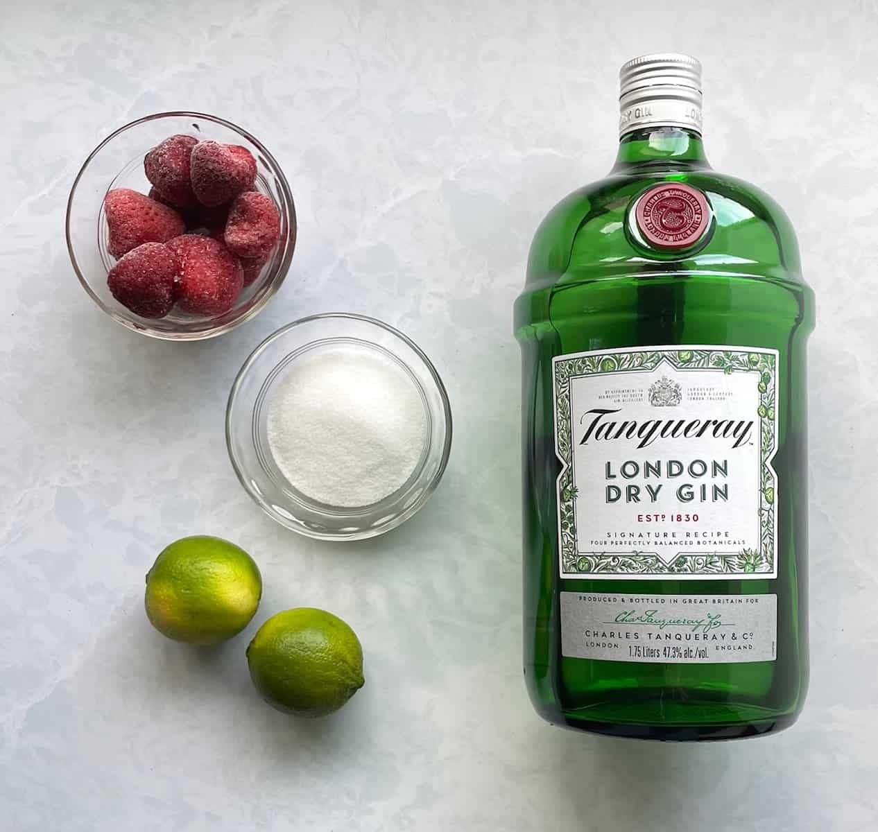 strawberries, sugar, limes, and bottle of Tanqueray London dry gin on a countertop.