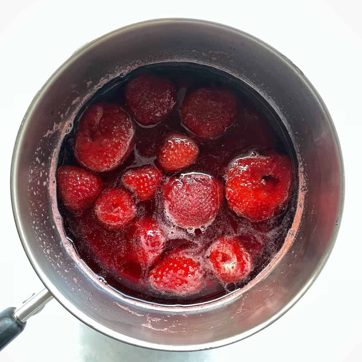 whole strawberries in a pot coated with red syrup.