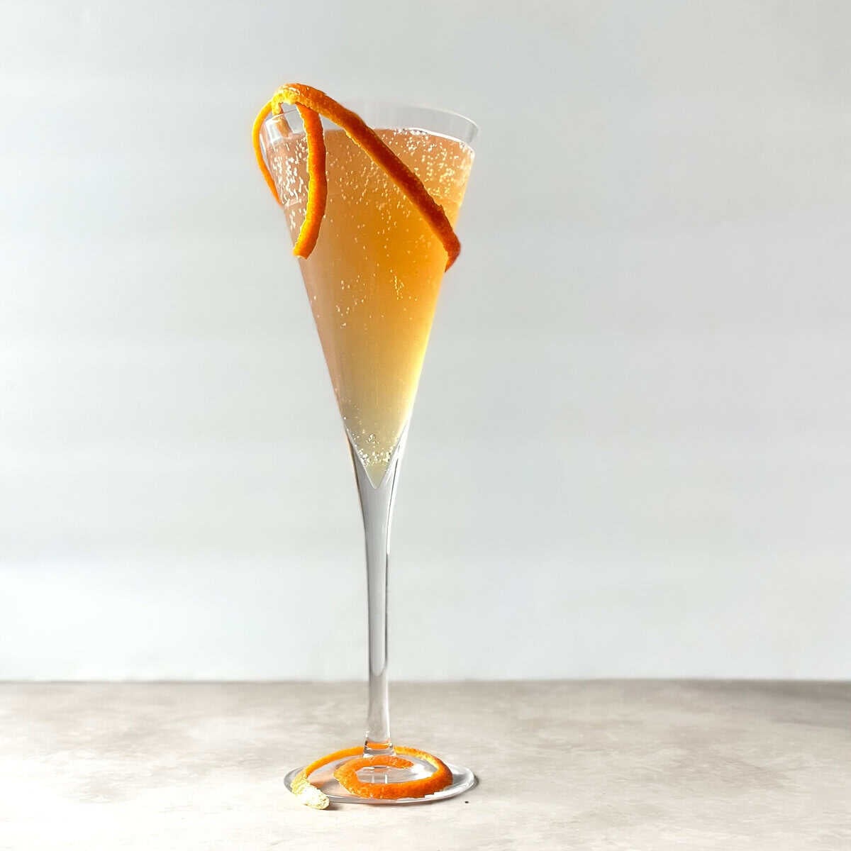 orange sparkling cocktail in a flute garnished with orange twist.
