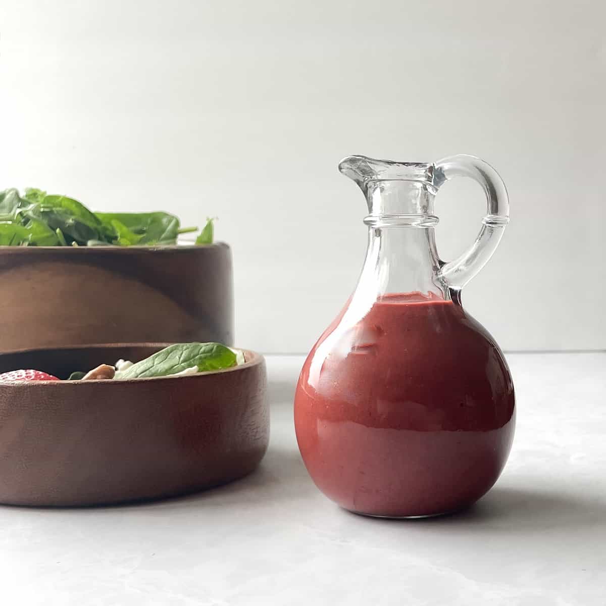 cherry red salad dressing next to small and large bowls of salad.