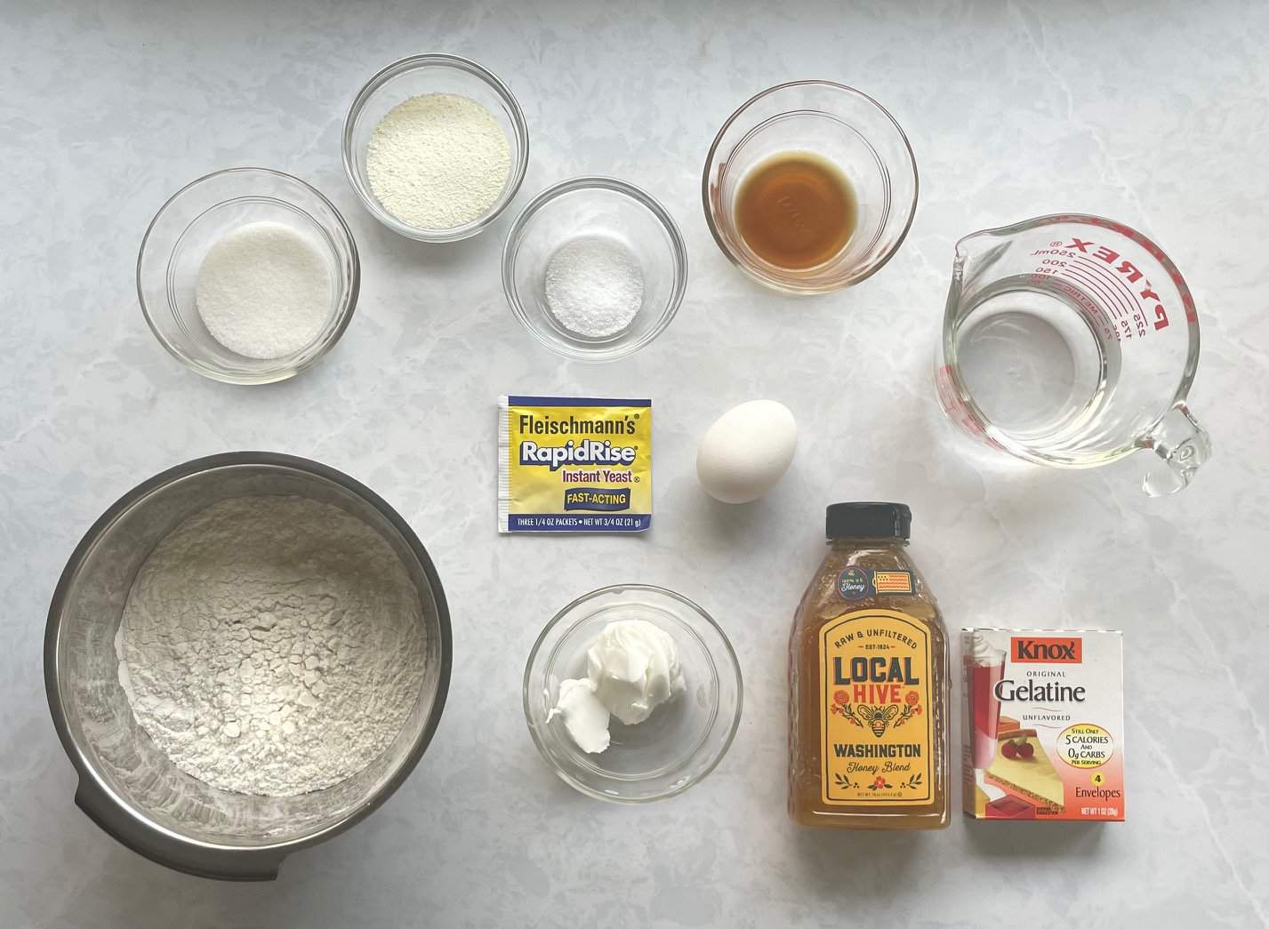 flour, sugar, milk powder, yeast, honey, and other ingredients on a countertop.