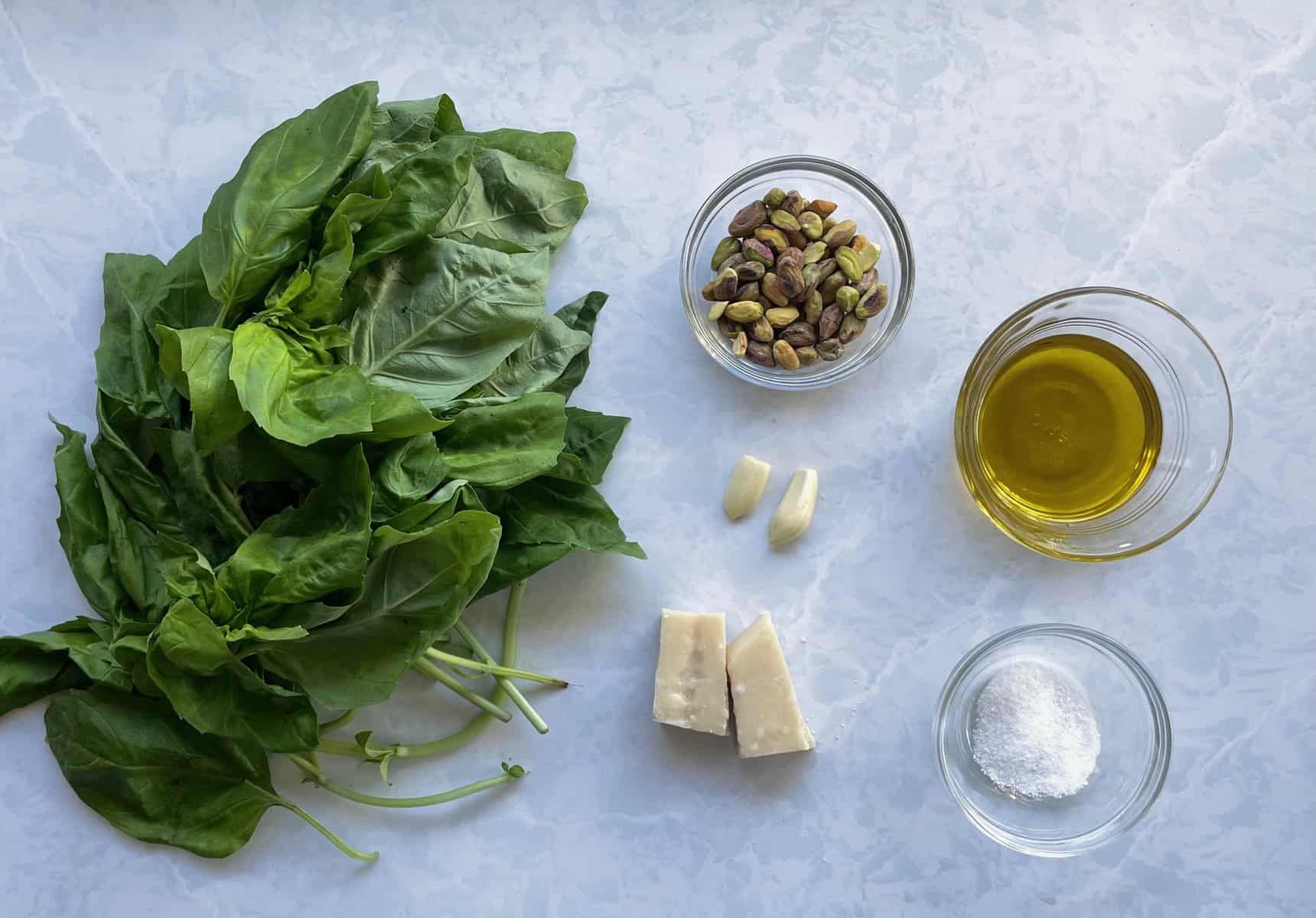 basil, pistachios, parmesan, garlic, olive oil, and salt on a countertop.