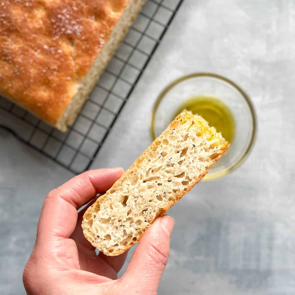 hand holding piece of black pepper focaccia dipped in olive oil.
