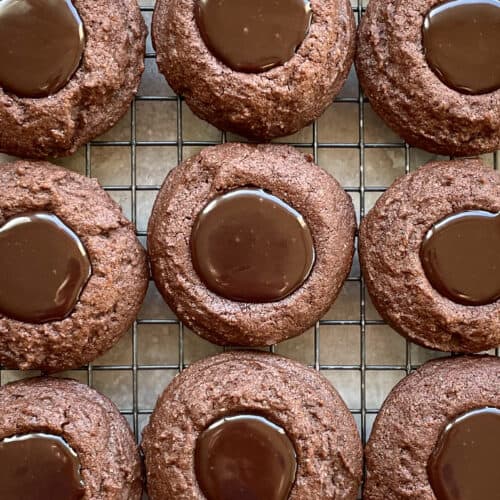 Nine brown thumbprint cookies filled with Nutella on a cooling rack.