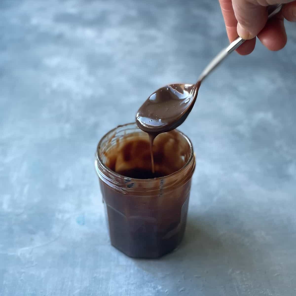 spoon dripping a dark brown sauce into a jam jar filled with the nutella ganache.