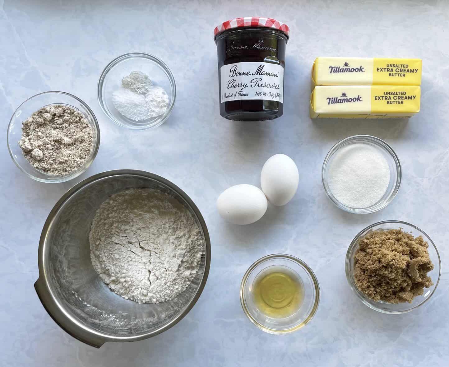 cherry jam, sugar, flour, almond flour, butter, eggs, and almond liqueur on a countertop.