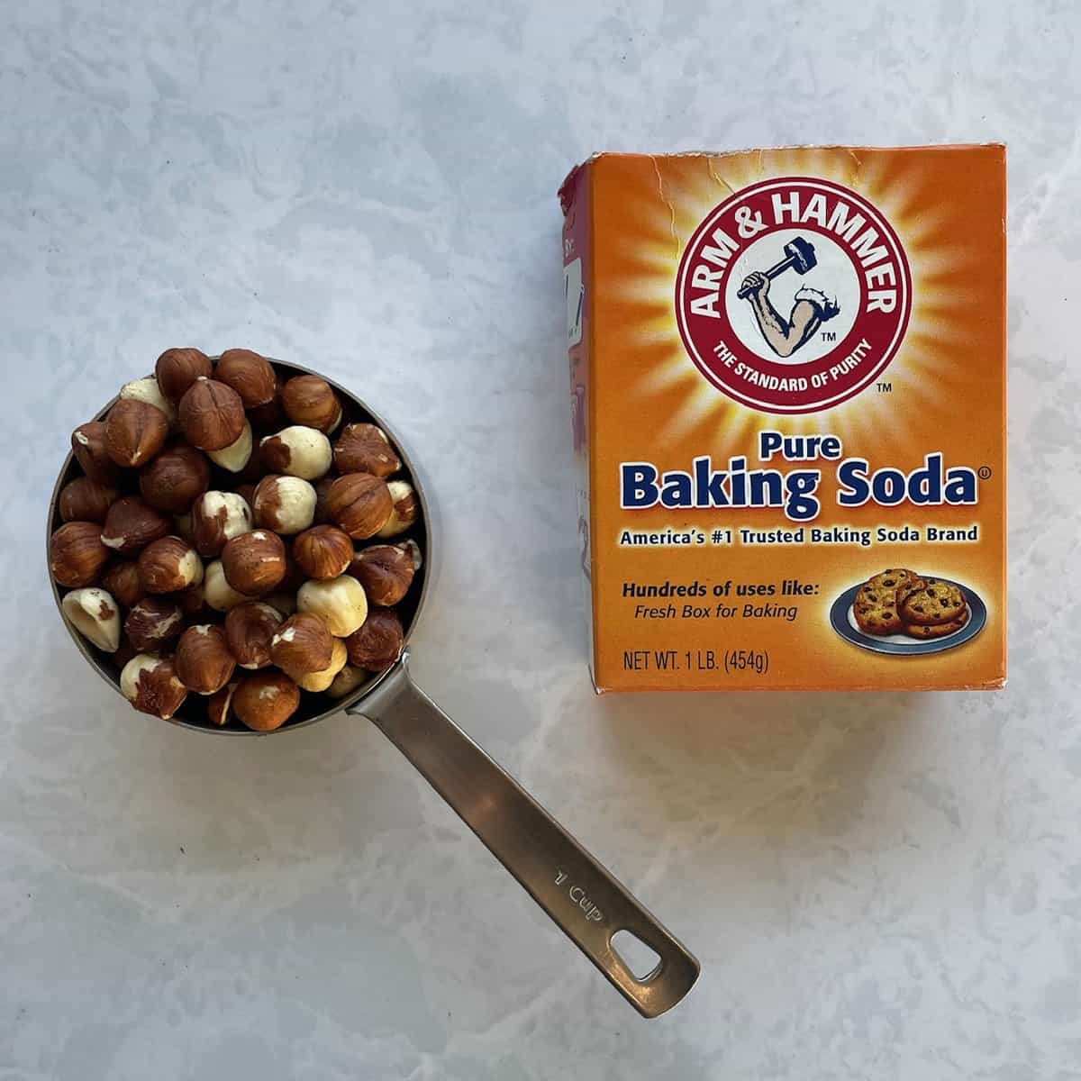 cup of unpeeled hazelnuts and box of baking soda on a countertop.