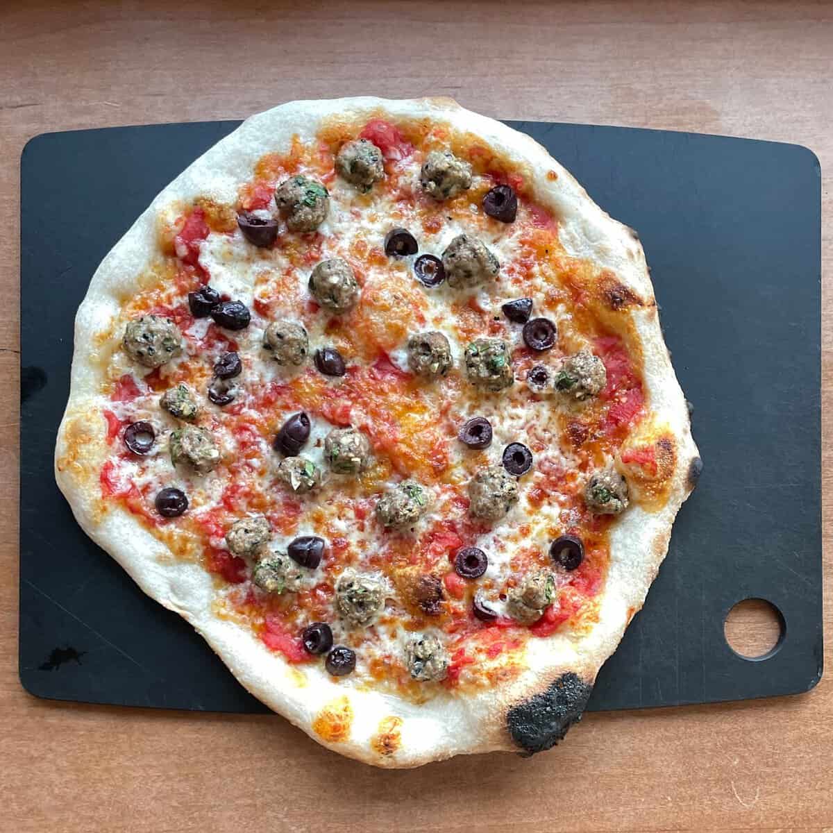 large pizza topped with tomato sauce, meatballs, and olives.