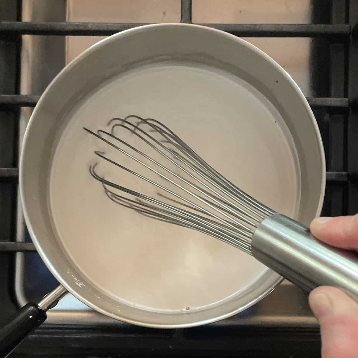 pot of white liquid on the stove with a whisk.