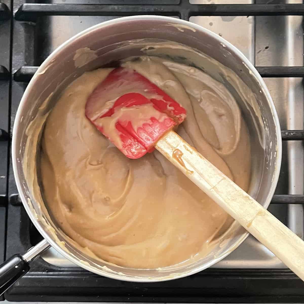 caramel colored pudding and a red silicone whisk in a small pot.