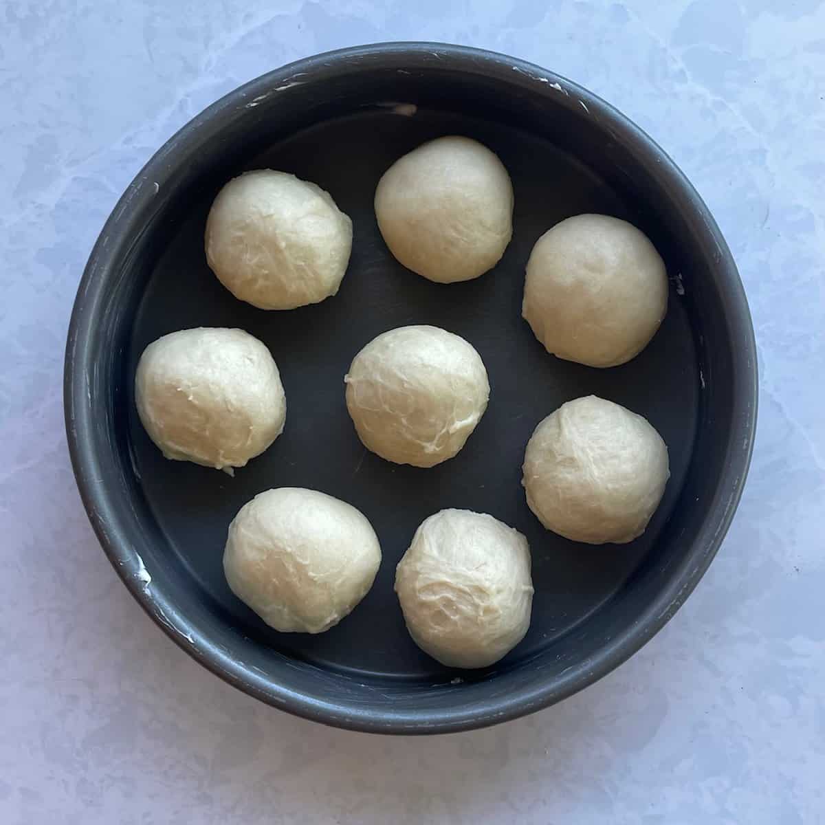 eight round balls of dough in a greased round cake pan.