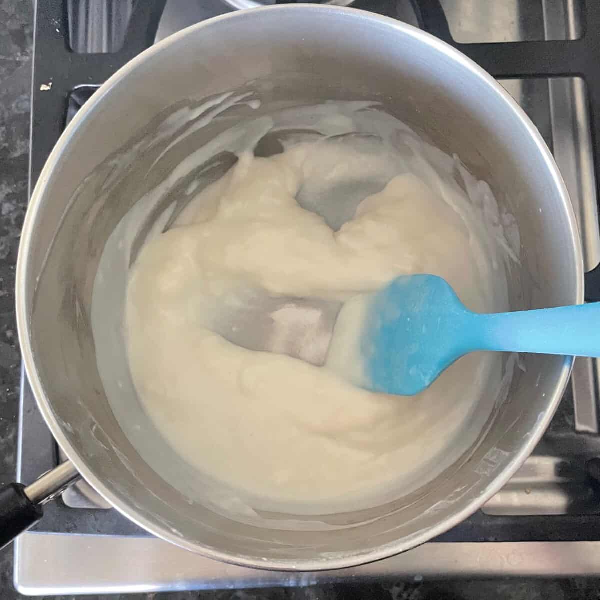 thick white roux in a metal pan with a path scraped away by a blue spatula.