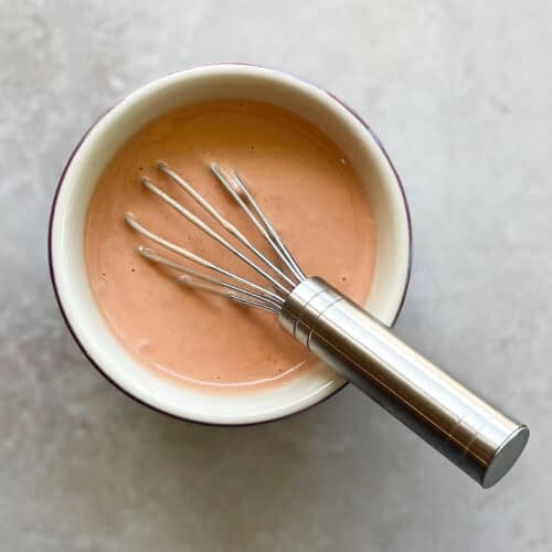 small bowl of salmon-colored. sauce with a metal whisk