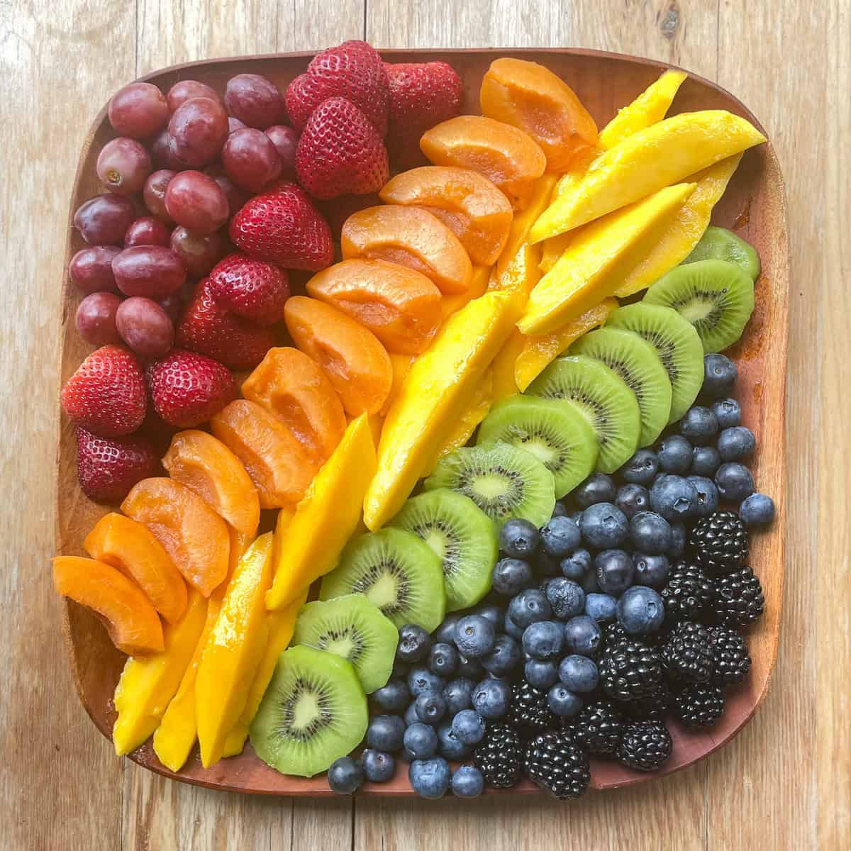 square wood platter with many fruit in rainbow order