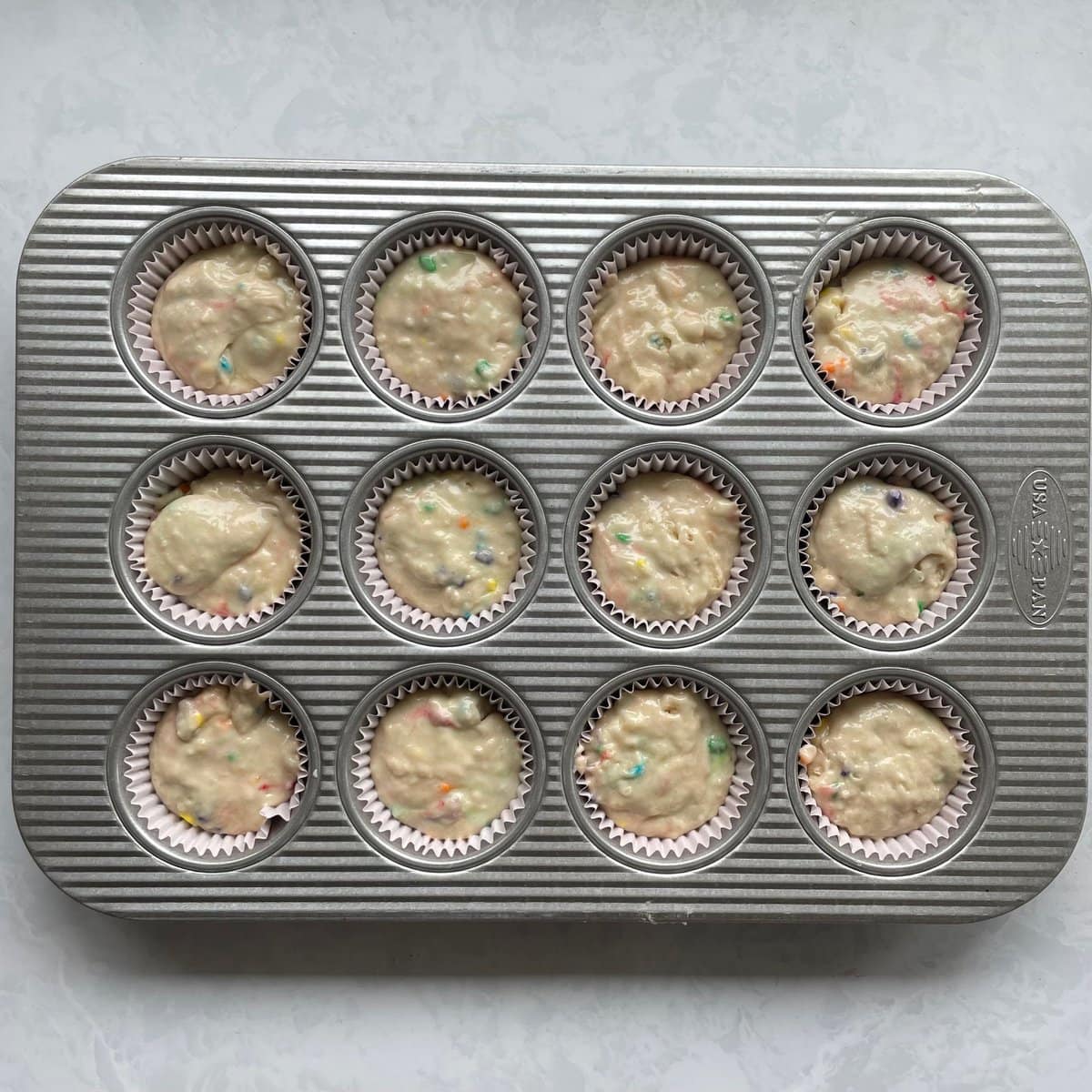 rainbow muffin batter in muffin tin.