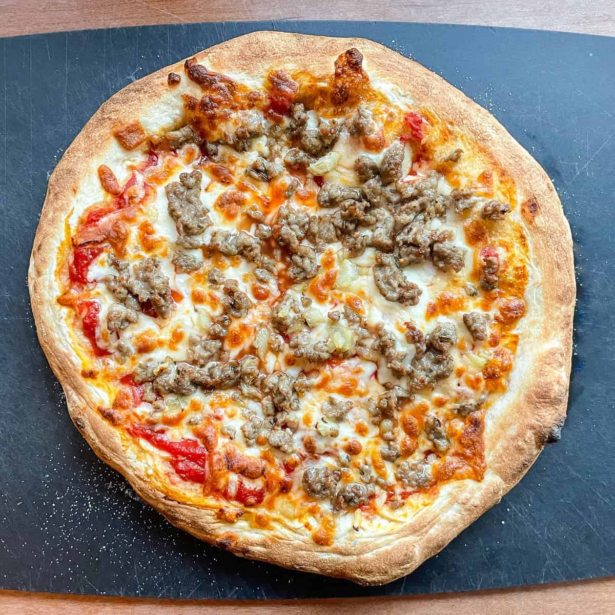 sausage and fennel Ooni pizza on a black cutting board.
