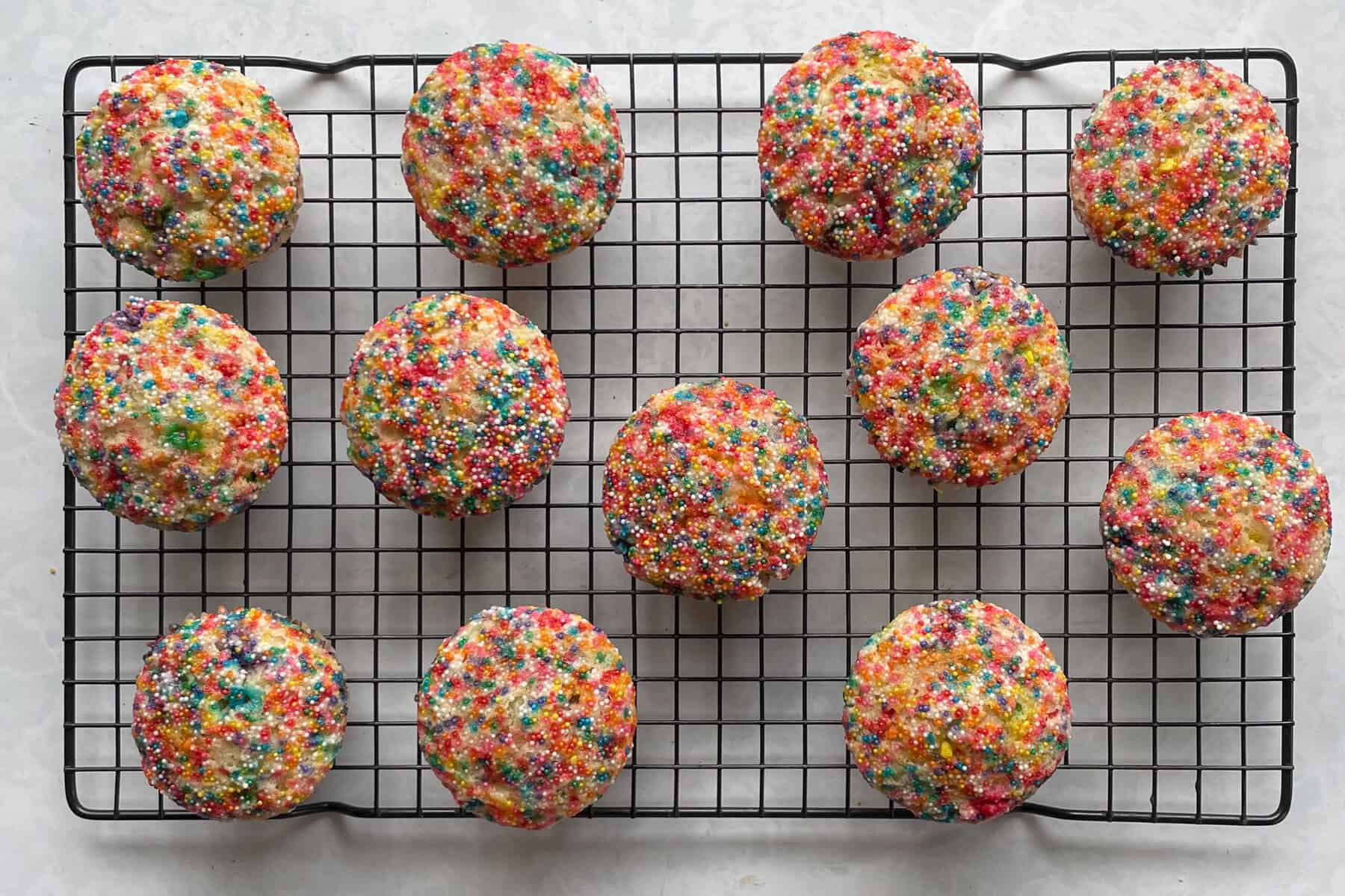 twelve rainbow sprinkle muffins on a cooling rack.