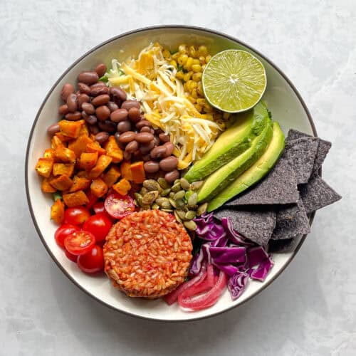 rainbow taco salad bowl with Mexican rice, tomatoes, sweet potato, beans, cheese, corn, lime, avocado, pepita, blue corn chips, purple cabbage, and pickled onions.