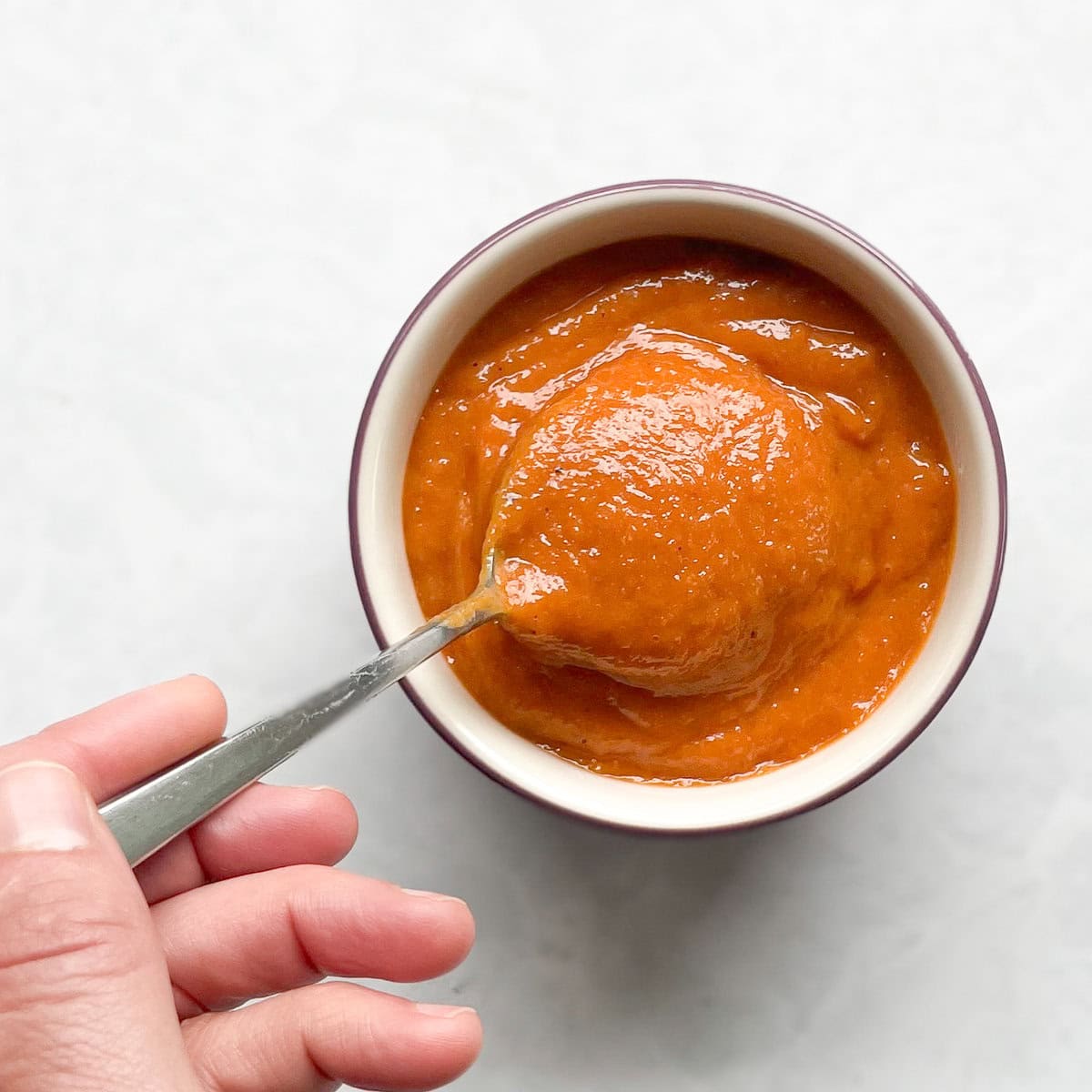 small bowl of bright orange sauce with a hand holding a dipping spoon. 