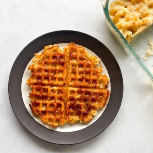 waffle made from macaroni on a plate next to a dish of cold mac and cheese.