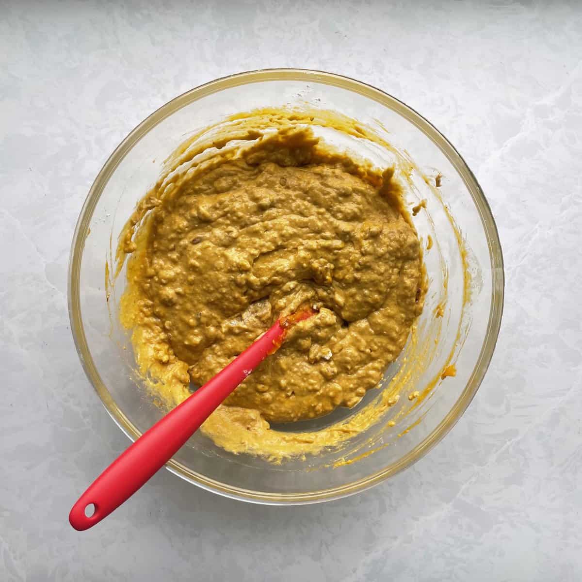 lumpy pecan pumpkin waffle batter with red spatula in glass bowl.